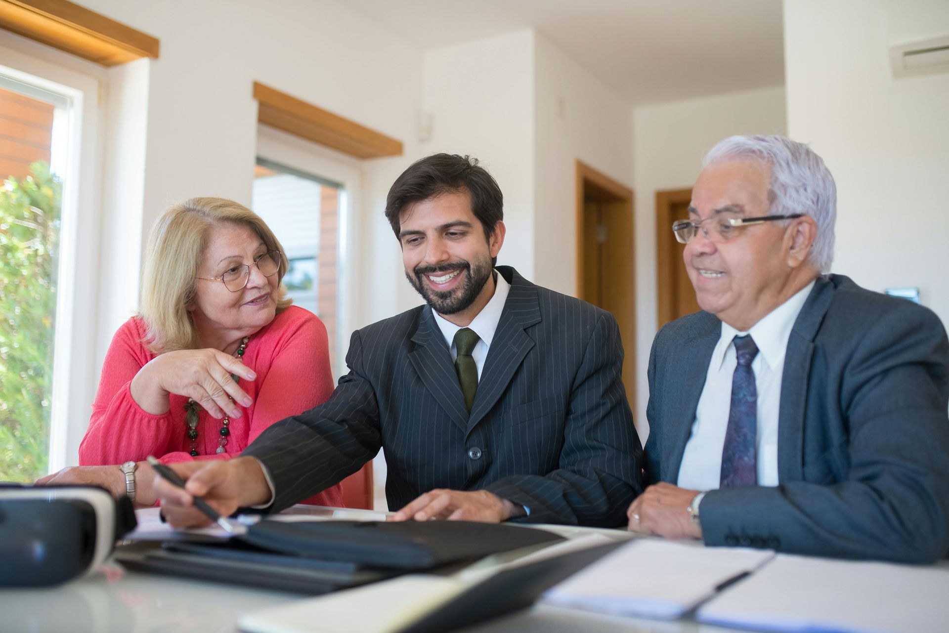 A financial advisor shows documents to an elderly couple at a table, all smiling indoors.